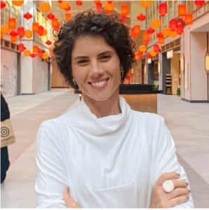 Retrato de Ana Luiza, cliente sorridente e de braços cruzados, validando sua excelente experiência. Depoimento real sobre a facilidade em encontrar o terno slim ideal para seu filho adolescente, destacando o atendimento exclusivo e com hora marcada na Ternos Curitiba, no Bairro Alto.